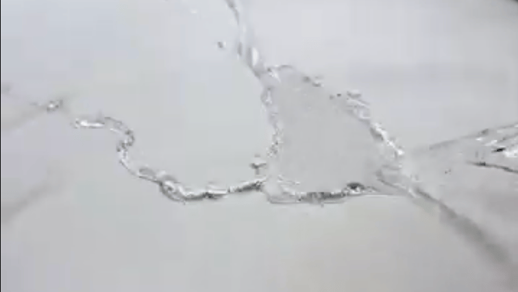 A close-up, monochromatic shot of clear liquid splashing across a flat surface.