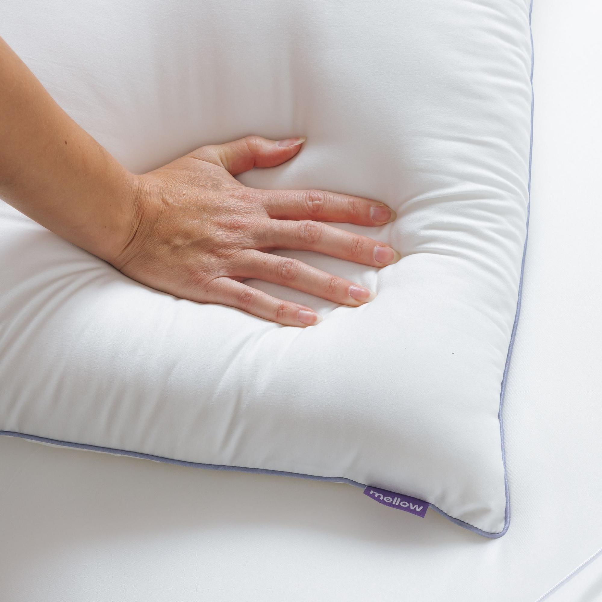 A hand pressing down on a white pillow with a purple tag that reads 'mellow'.
