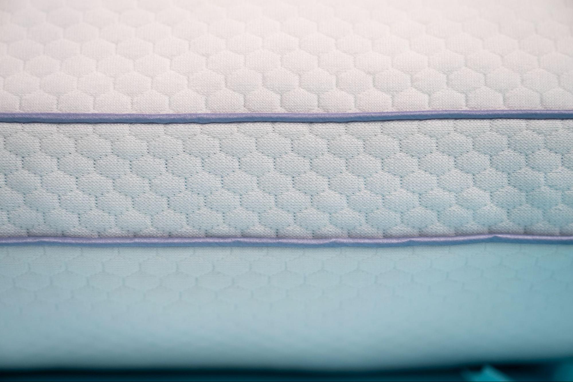A close-up of a white and light blue quilted fabric with a hexagonal pattern and purple piping.
