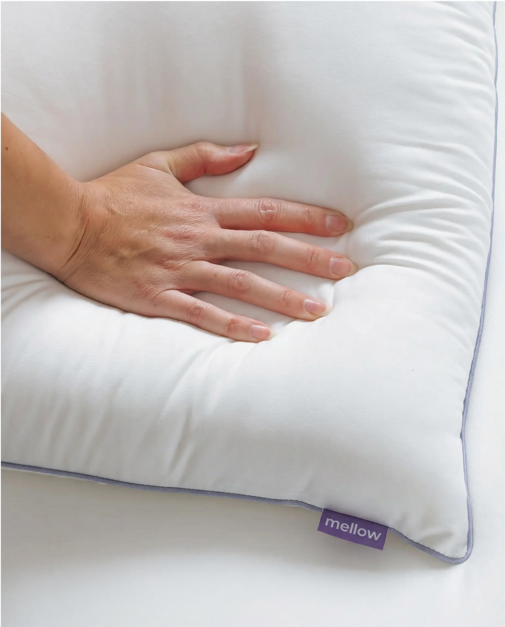 A close-up of a hand pressing into a plush white pillow with a purple tag that says 'mellow'.
