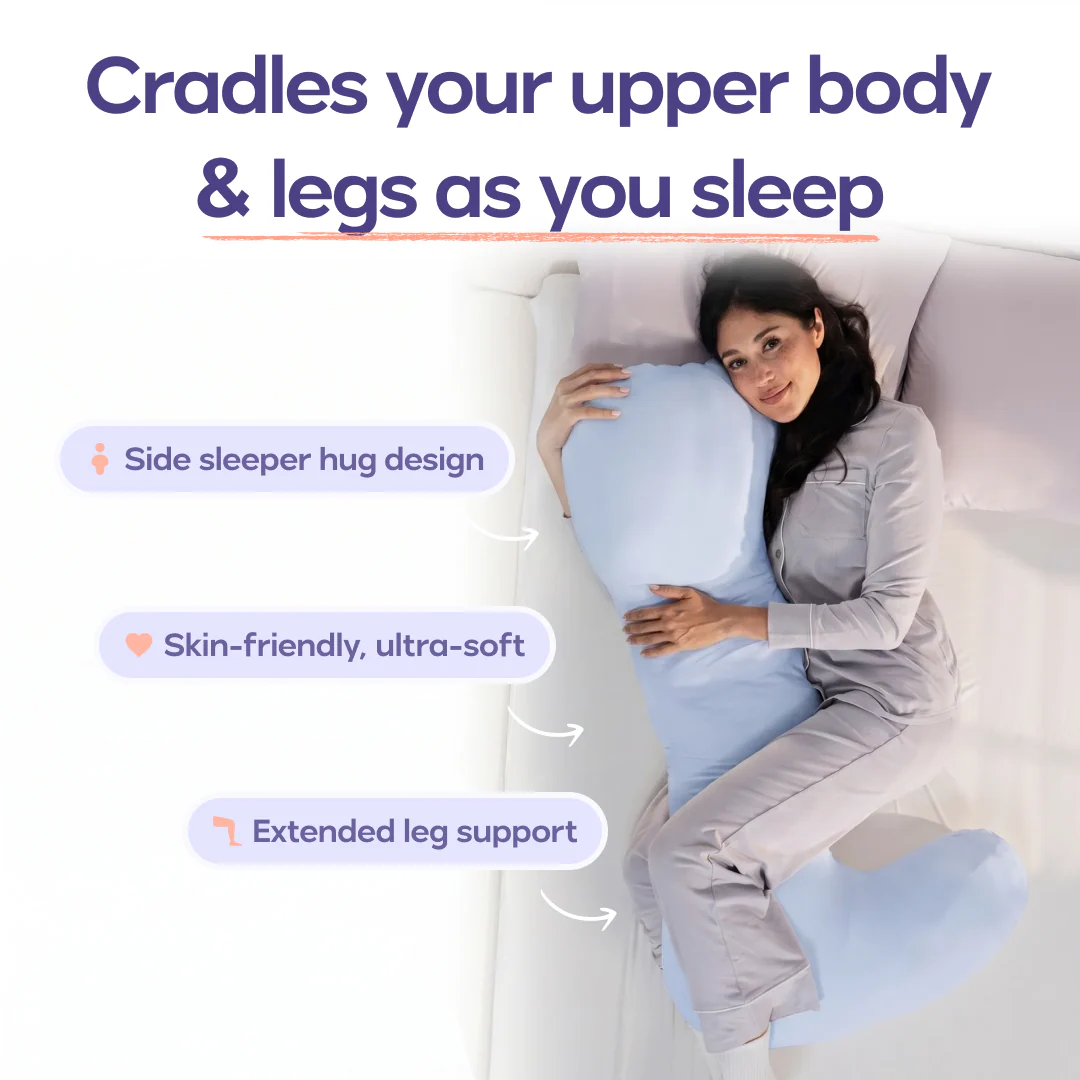 A woman in pajamas smiles while cuddling a large, light blue body pillow in bed.