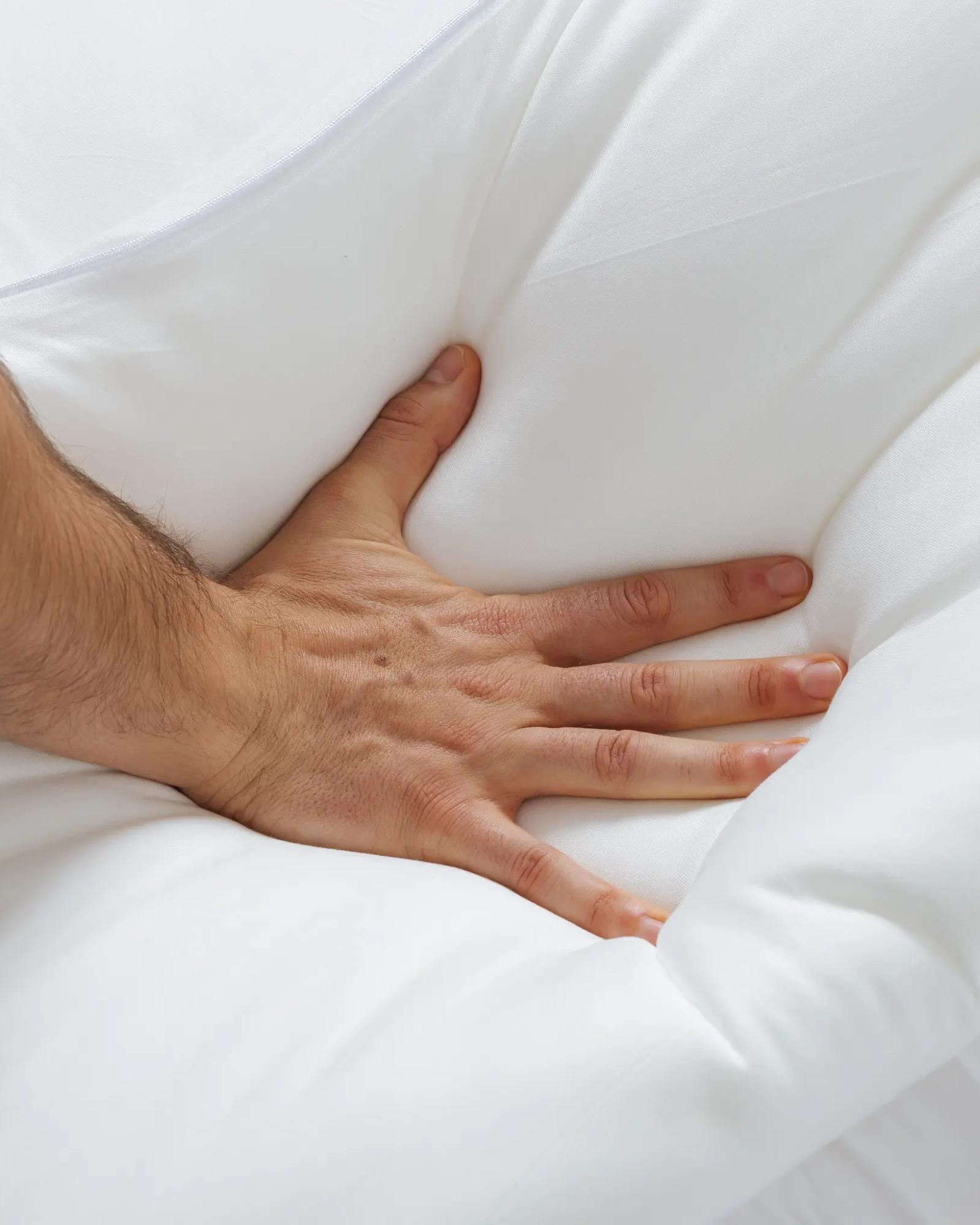 A close-up of a person's hand pressing into a fluffy white comforter or mattress topper.