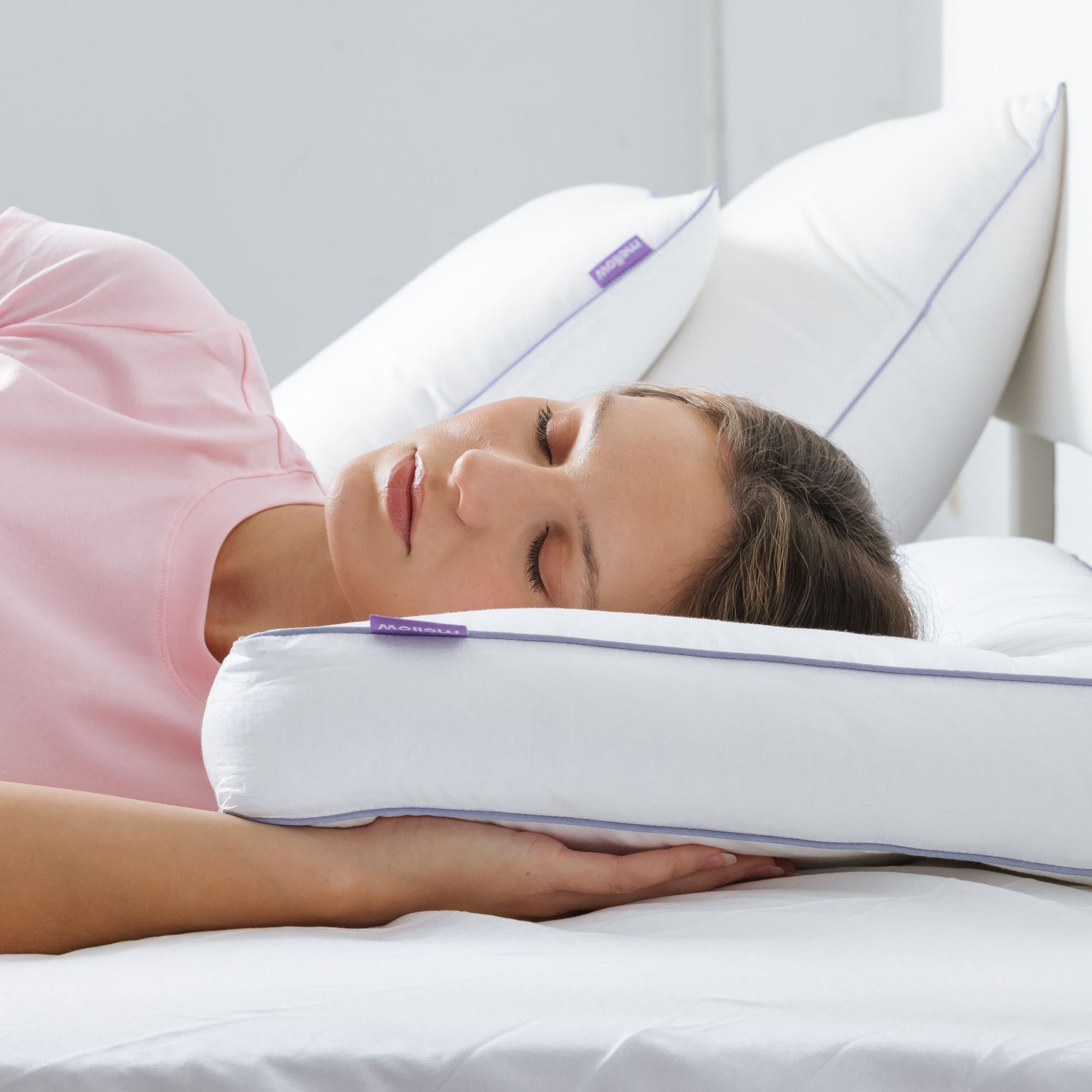 A woman in a pink shirt sleeping on her side on a white pillow with purple accents.