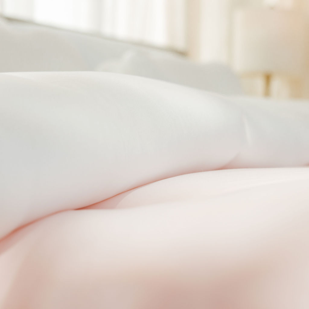 A close-up, soft-focus view of a white comforter layered on top of a pink comforter.