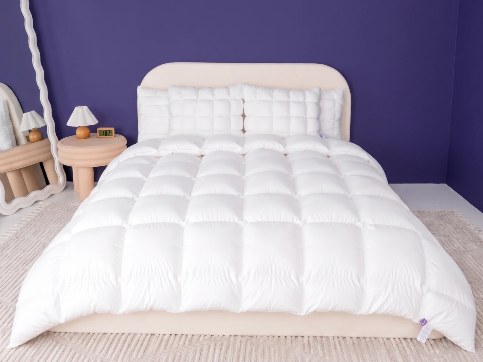 A bed with a white quilted comforter and matching pillows against a solid purple wall.