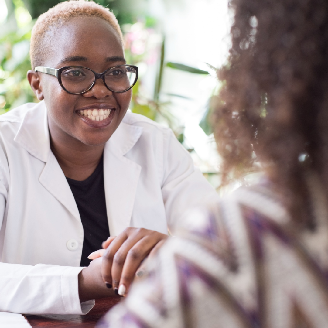 Smiling person in glasses and lab coat talking to someone.