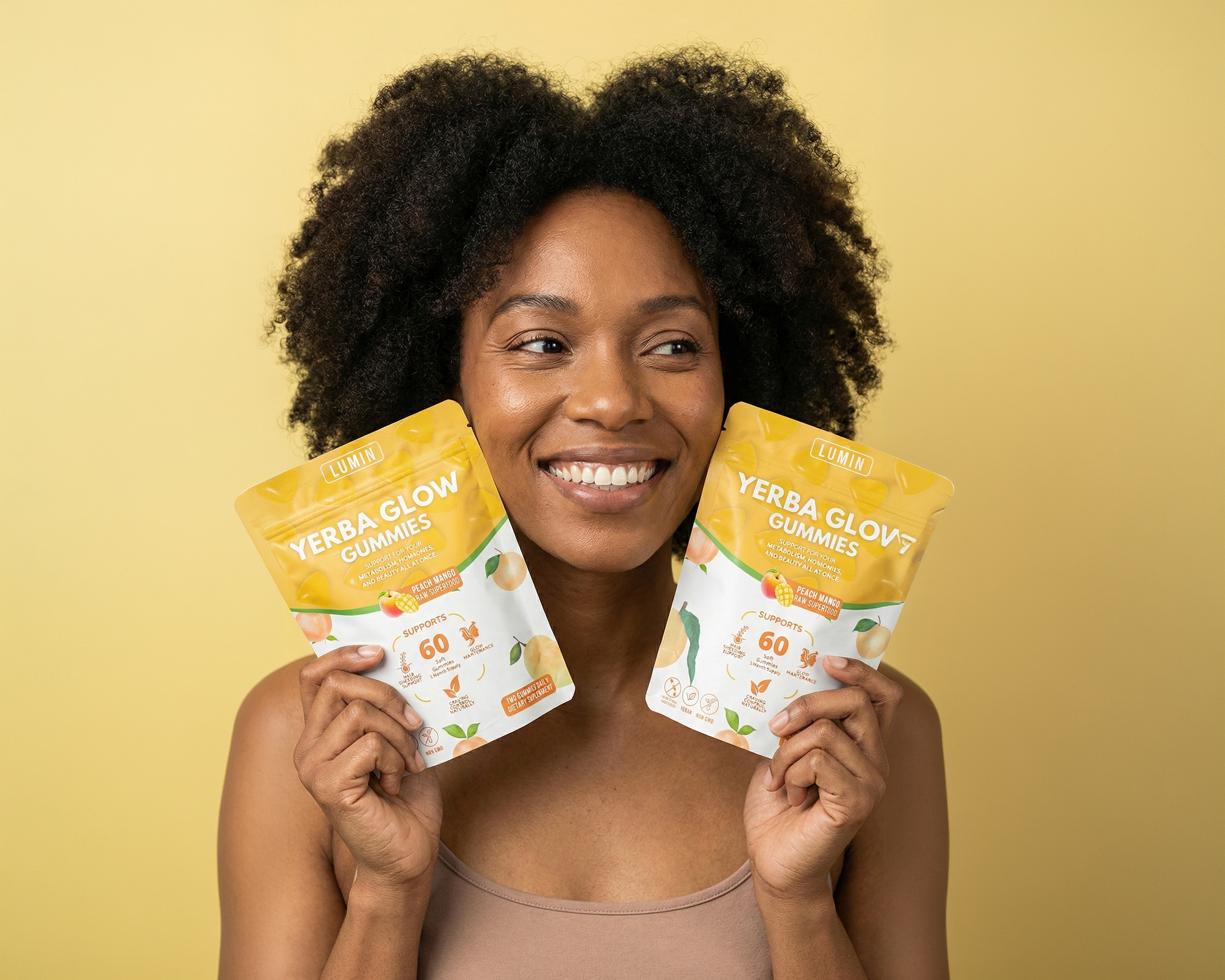 A smiling Black woman with an afro holds two pouches of Lumin Yerba Glow Gummies against a yellow background.