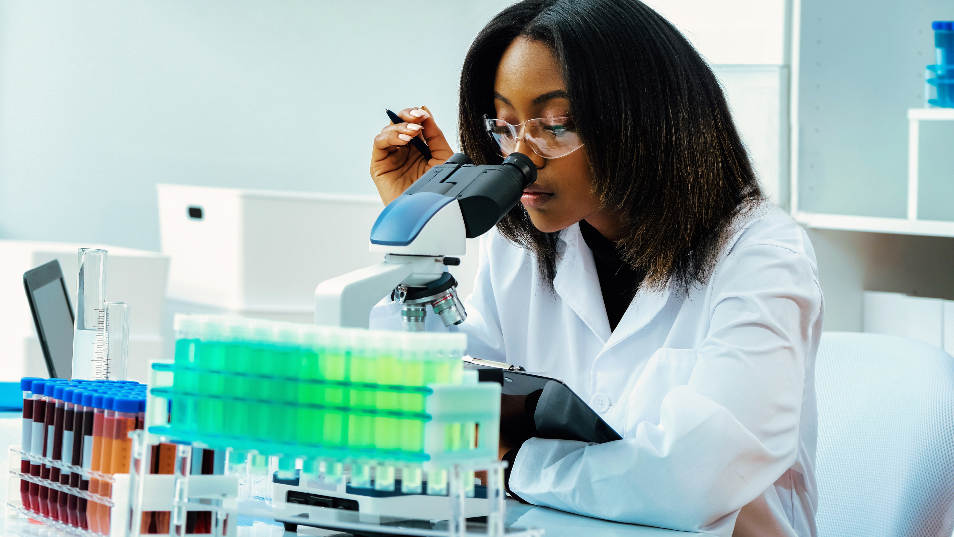 Person in lab coat examining samples under a microscope in a laboratory.