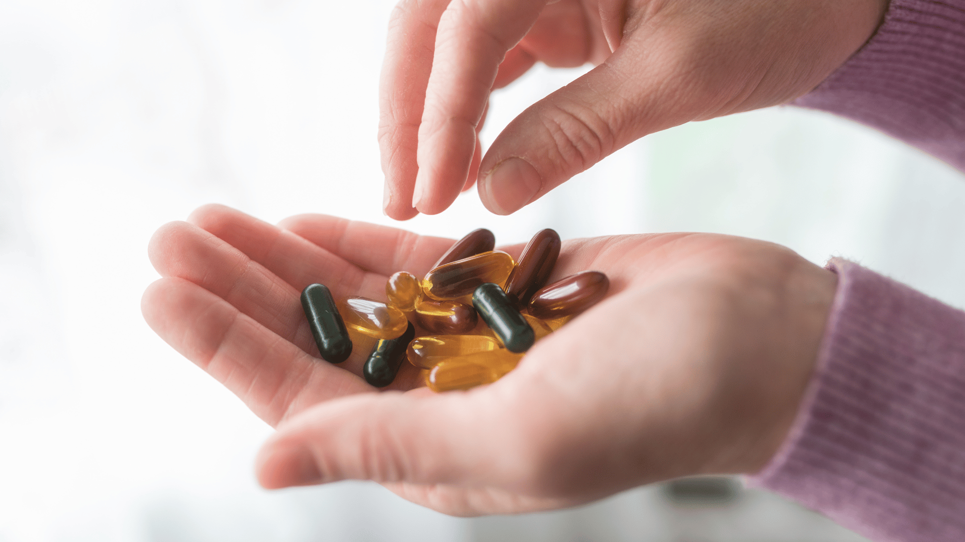 Hands holding various colored capsules and pills.