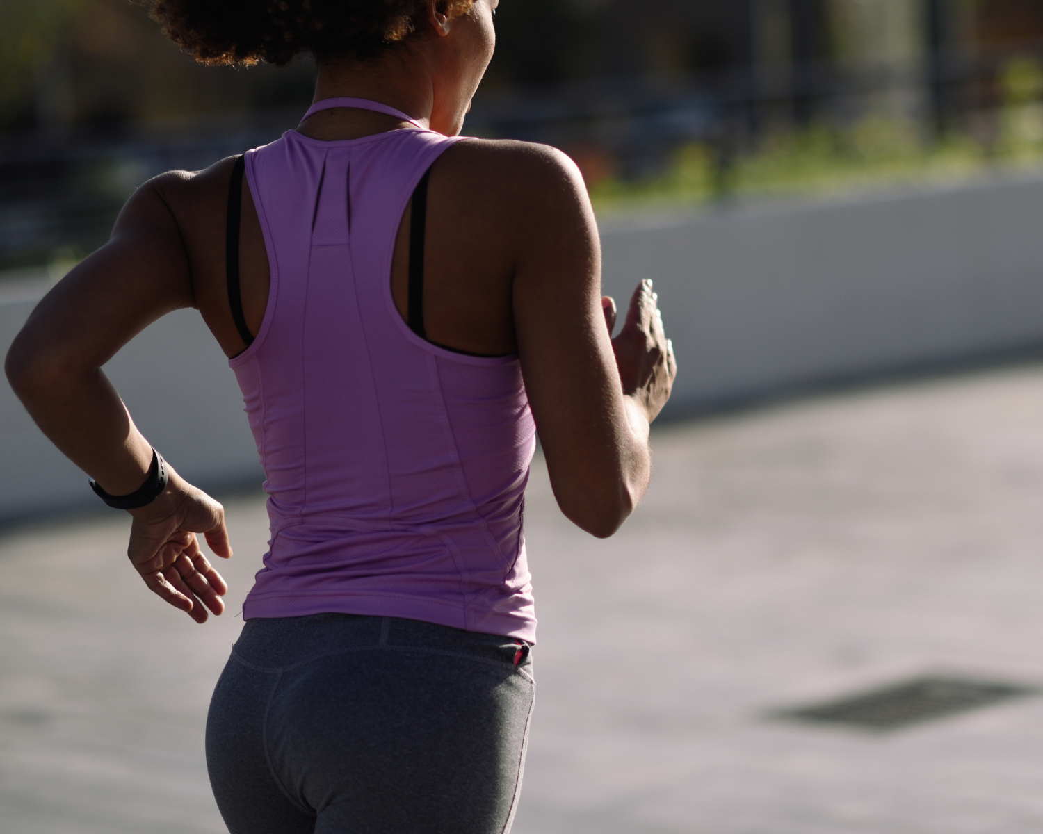 Rear view of a woman in a purple athletic top and grey leggings running outdoors.