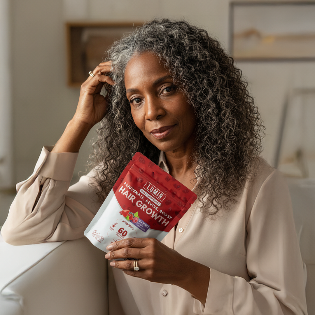 A woman with curly gray hair holds a pouch of Lumin Hair Growth supplement.