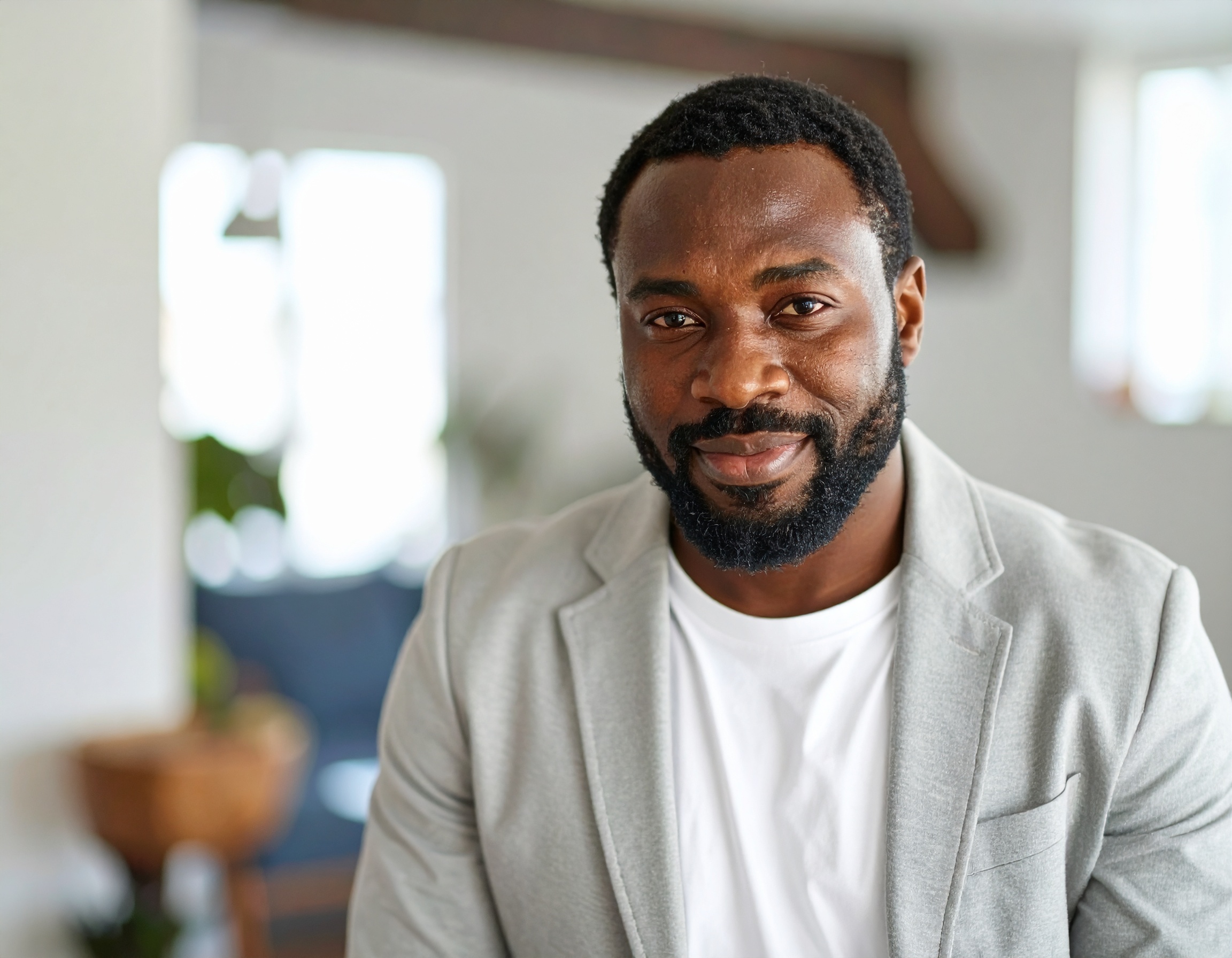 Man in a light gray blazer smiling indoors.