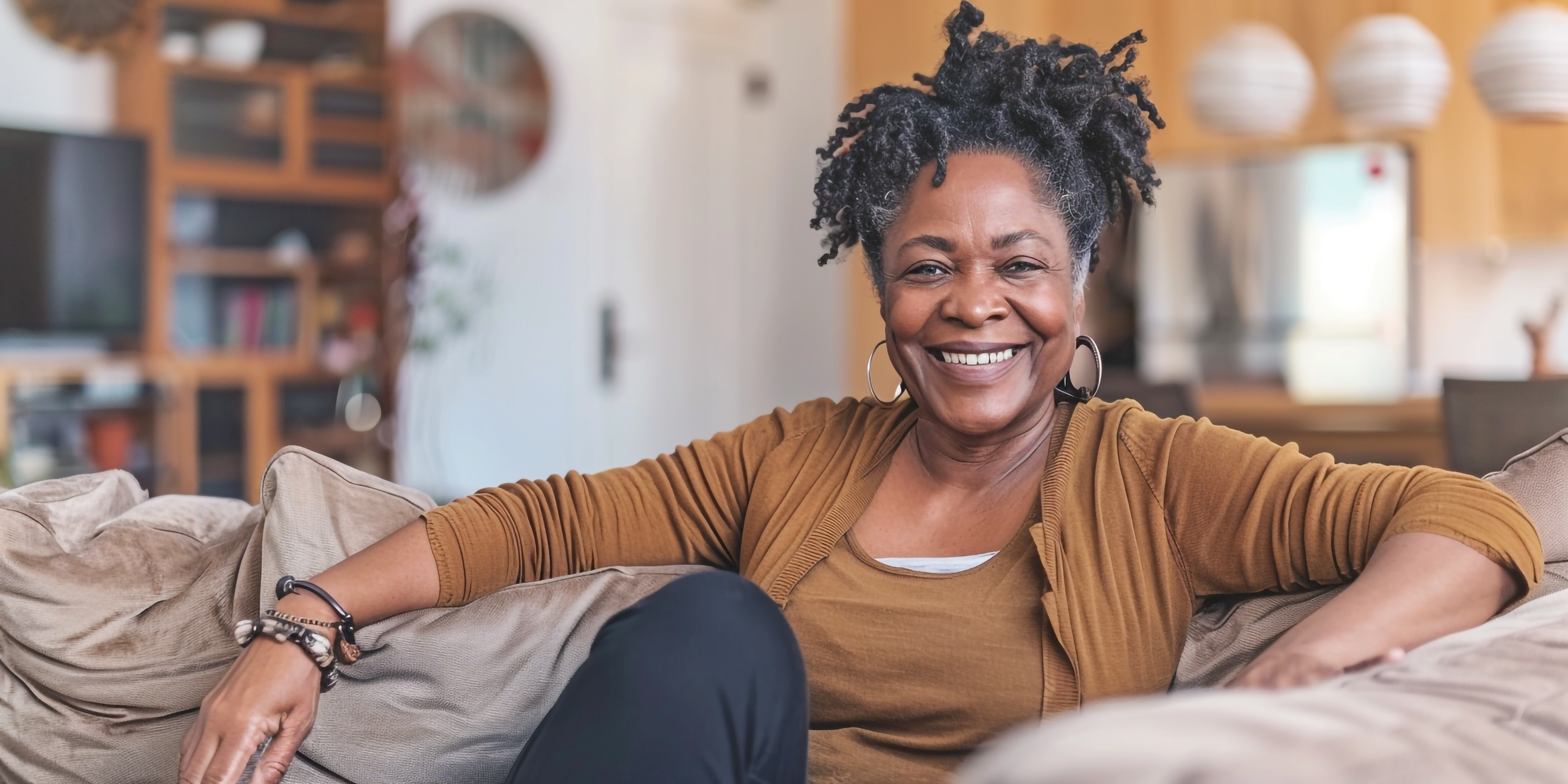 Smiling person sitting on a couch in a cozy living room.