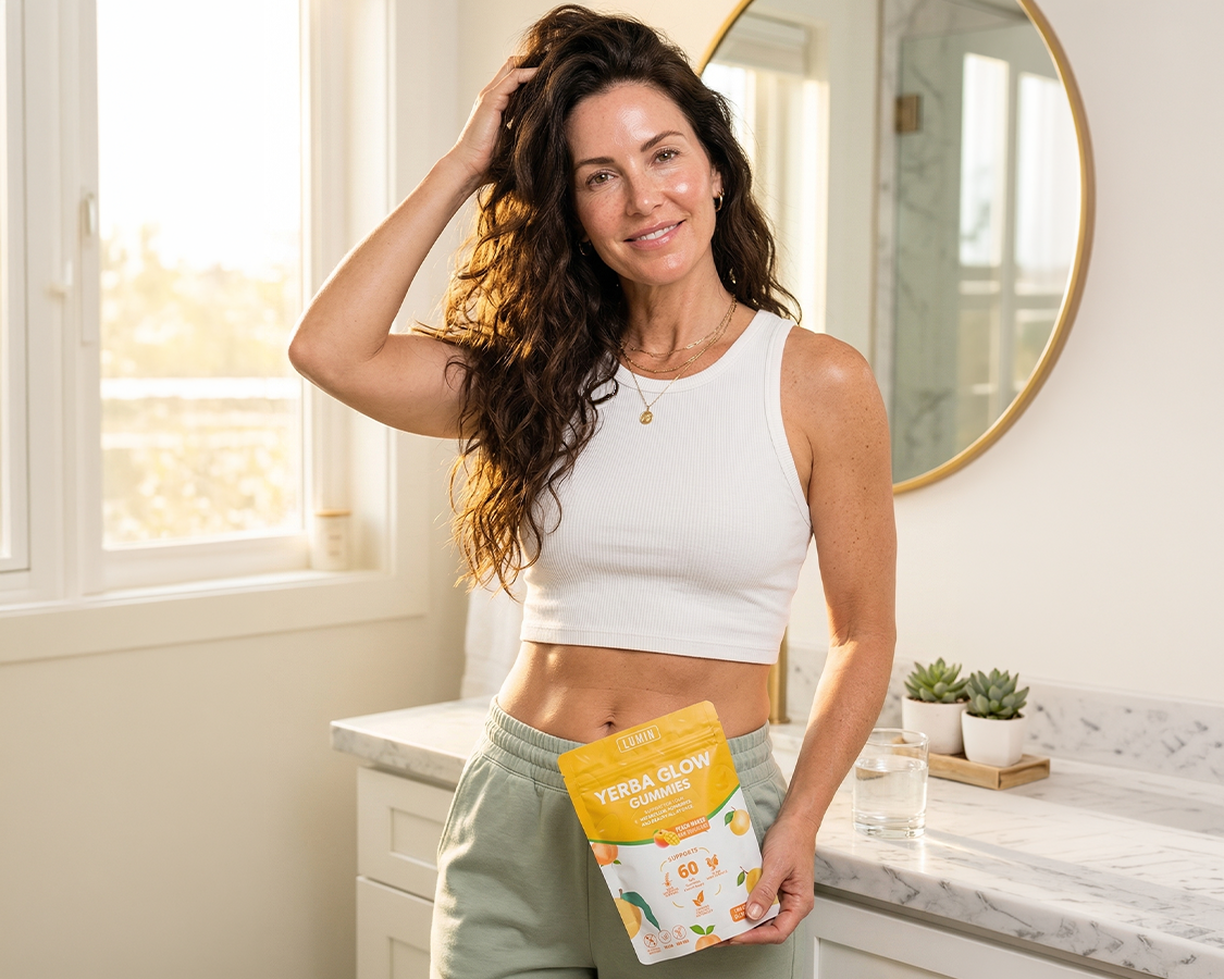 A woman with long, wavy hair holds a pouch of Yerba Glow Gummies while standing in a bathroom.