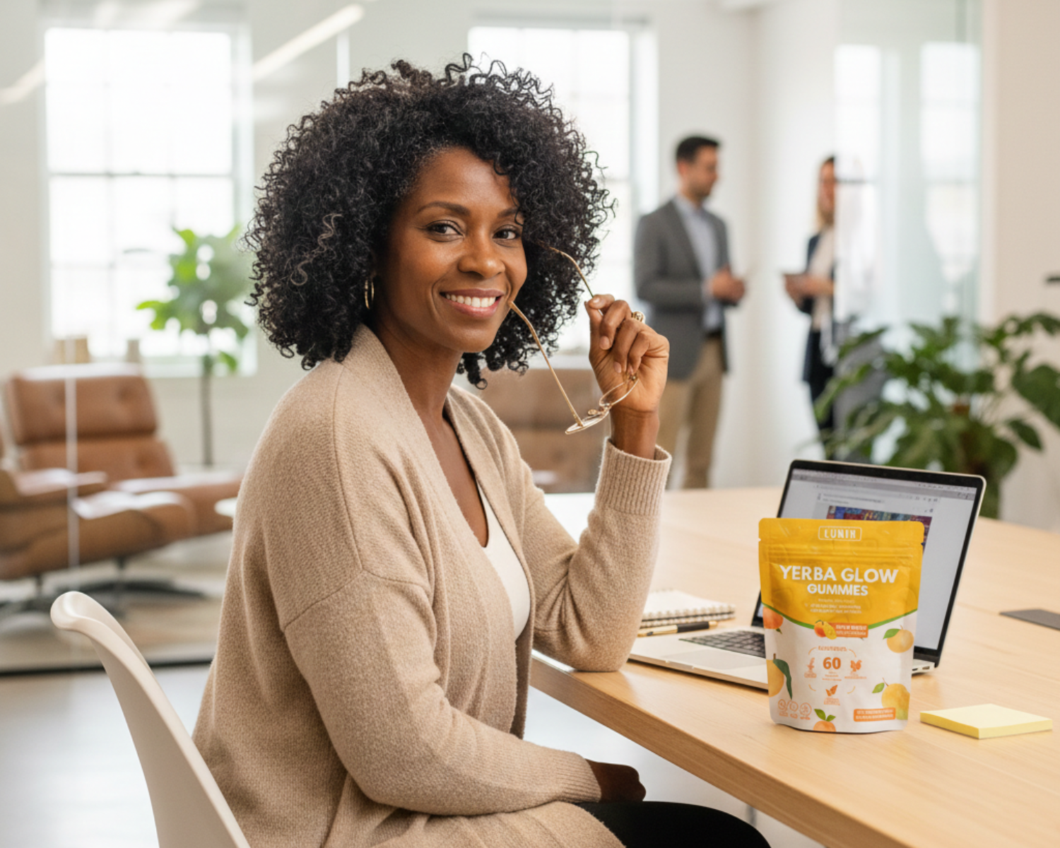 A woman sits at an office desk with a laptop and a pouch of Yerba Glow Gummies.