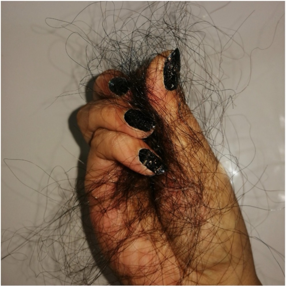 Woman with striped shirt looking in mirror, touching her hair.
