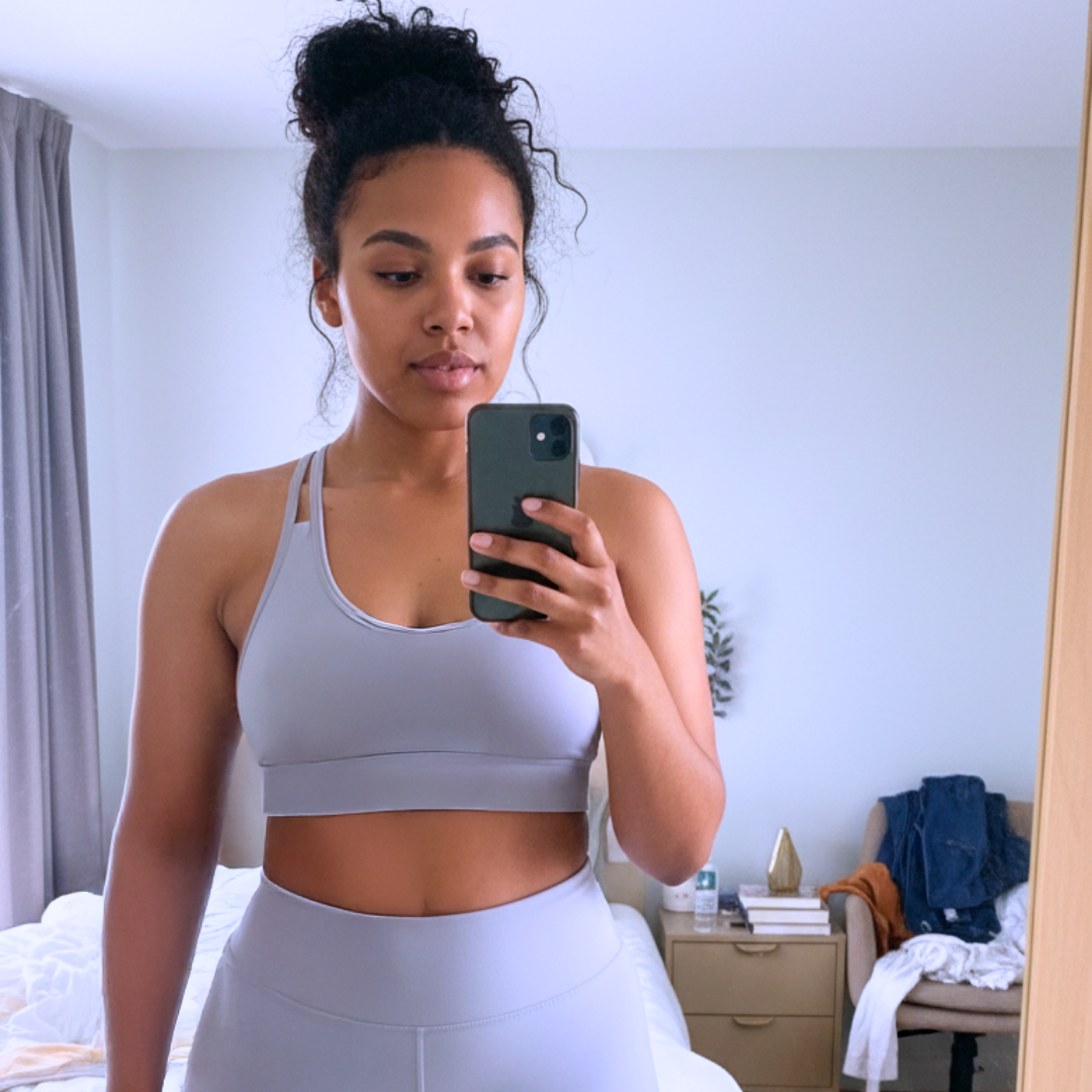 Person in activewear taking a mirror selfie in a bedroom.
