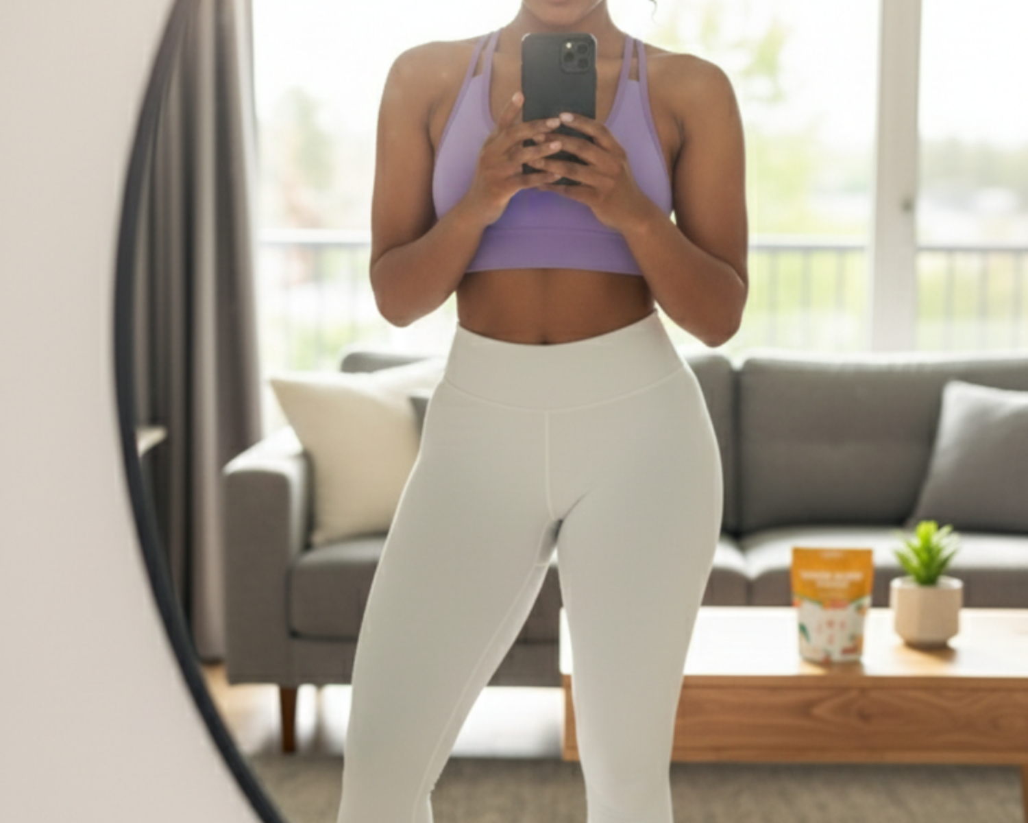 A person in a purple sports bra and white leggings takes a selfie in a mirror.