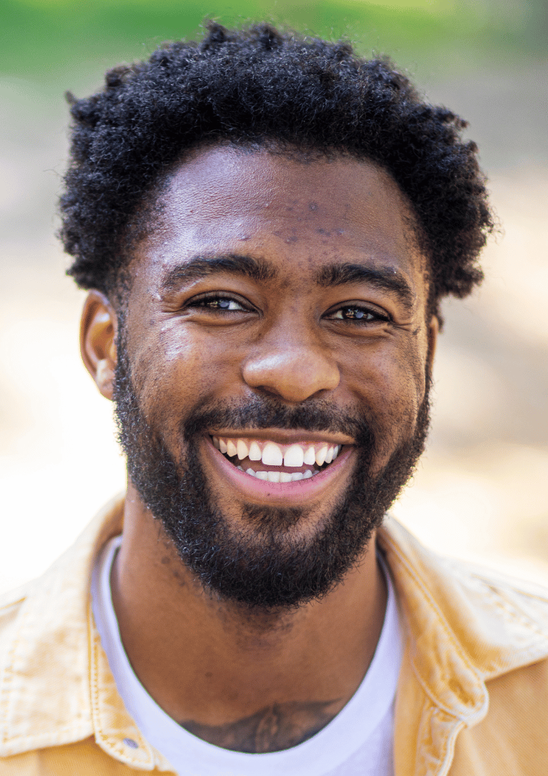 Smiling man with a beard and curly hair, wearing a yellow jacket.