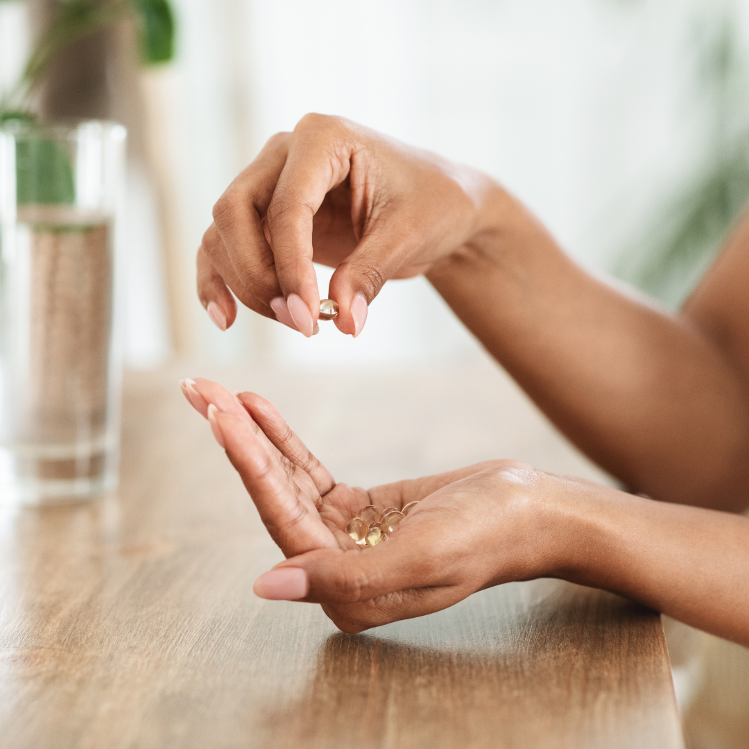 Hands holding and picking up vitamin capsules on a wooden surface.