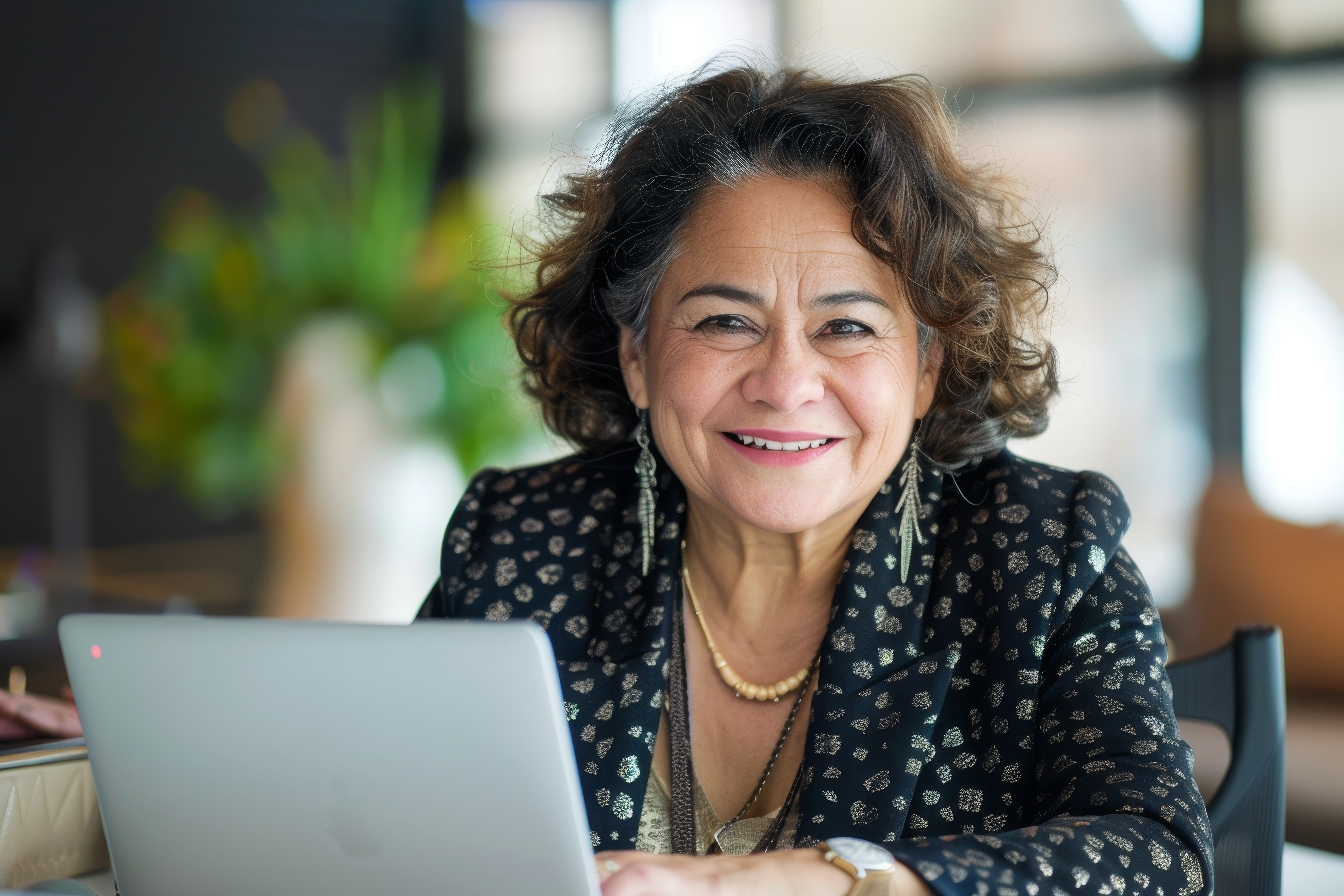 Smiling person with curly hair using a laptop indoors.