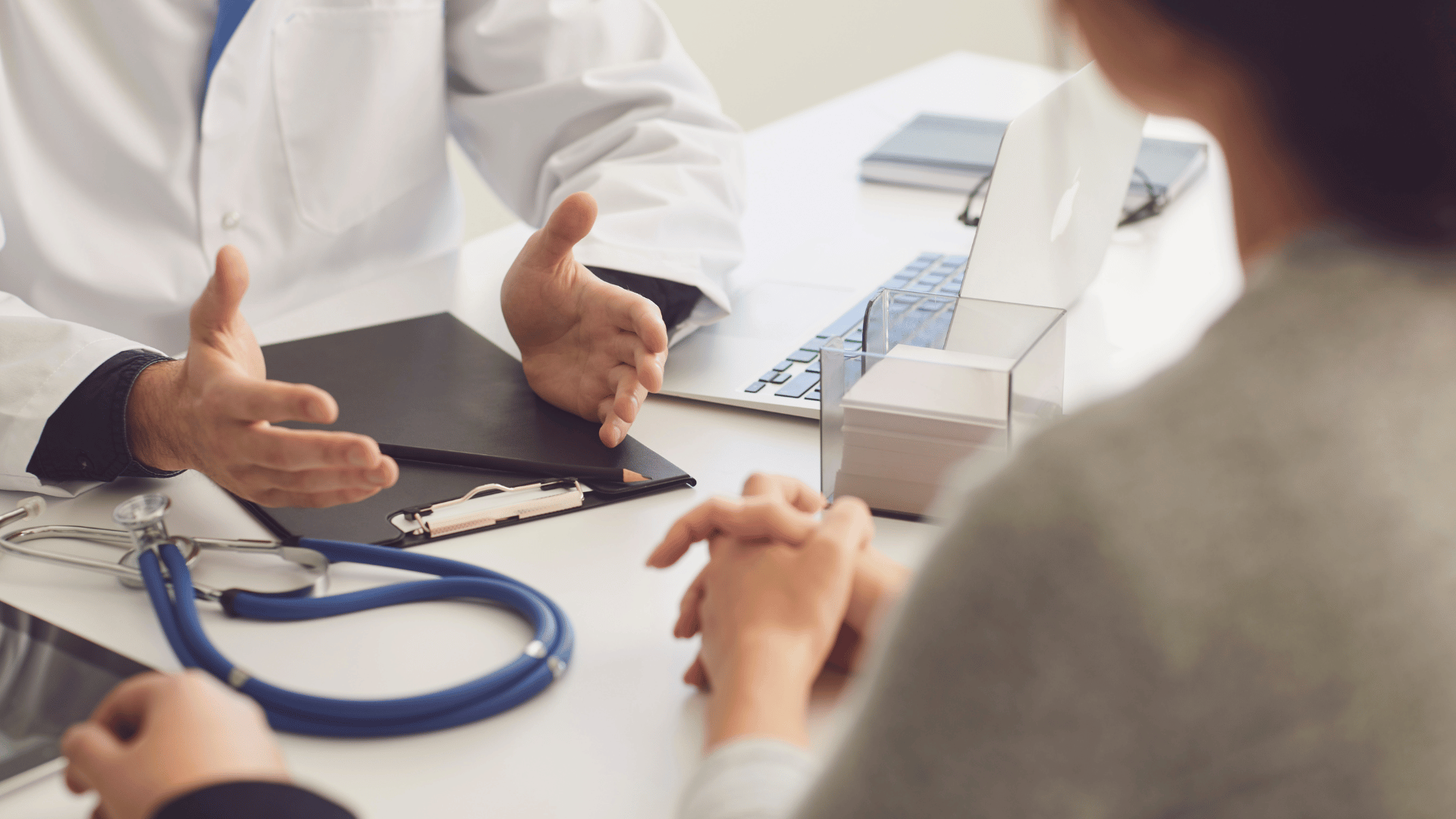 Doctor and patient discussing at a desk with a stethoscope and clipboard.