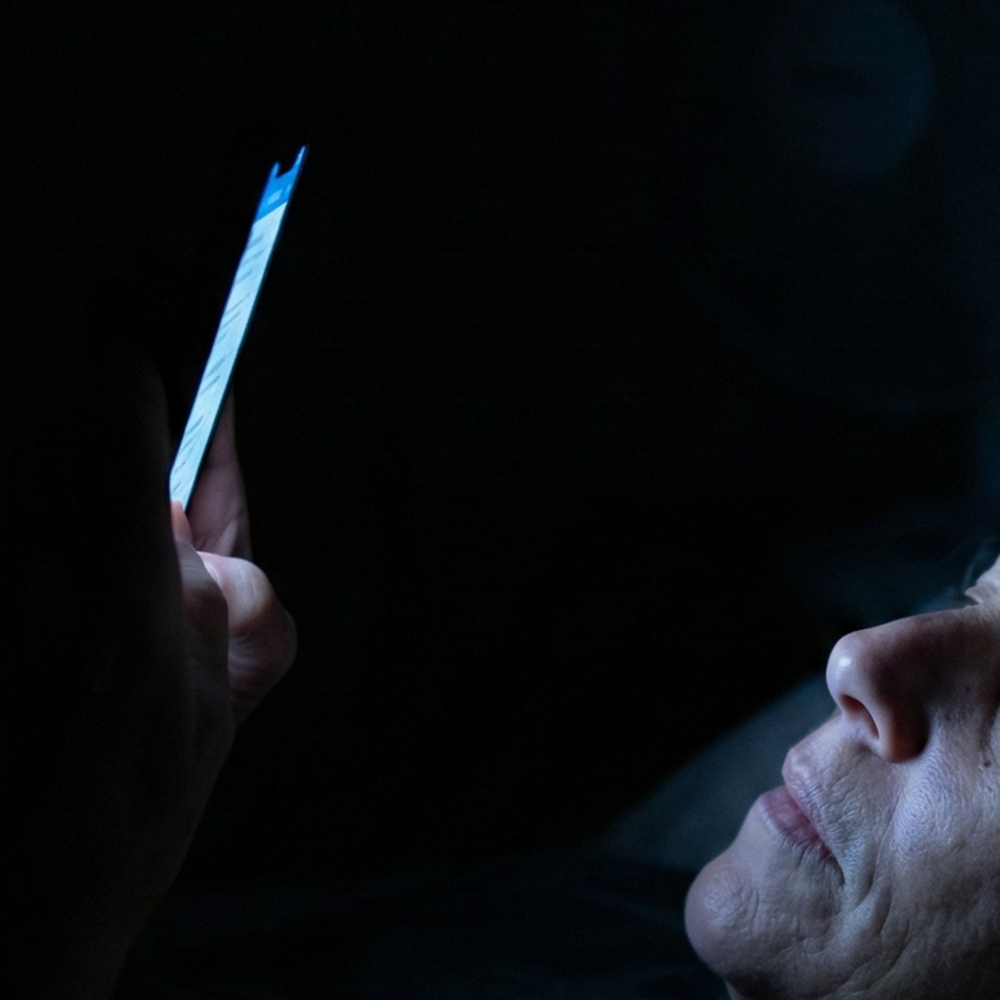 Close-up of a person's face illuminated by the glow of a smartphone screen in the dark.
