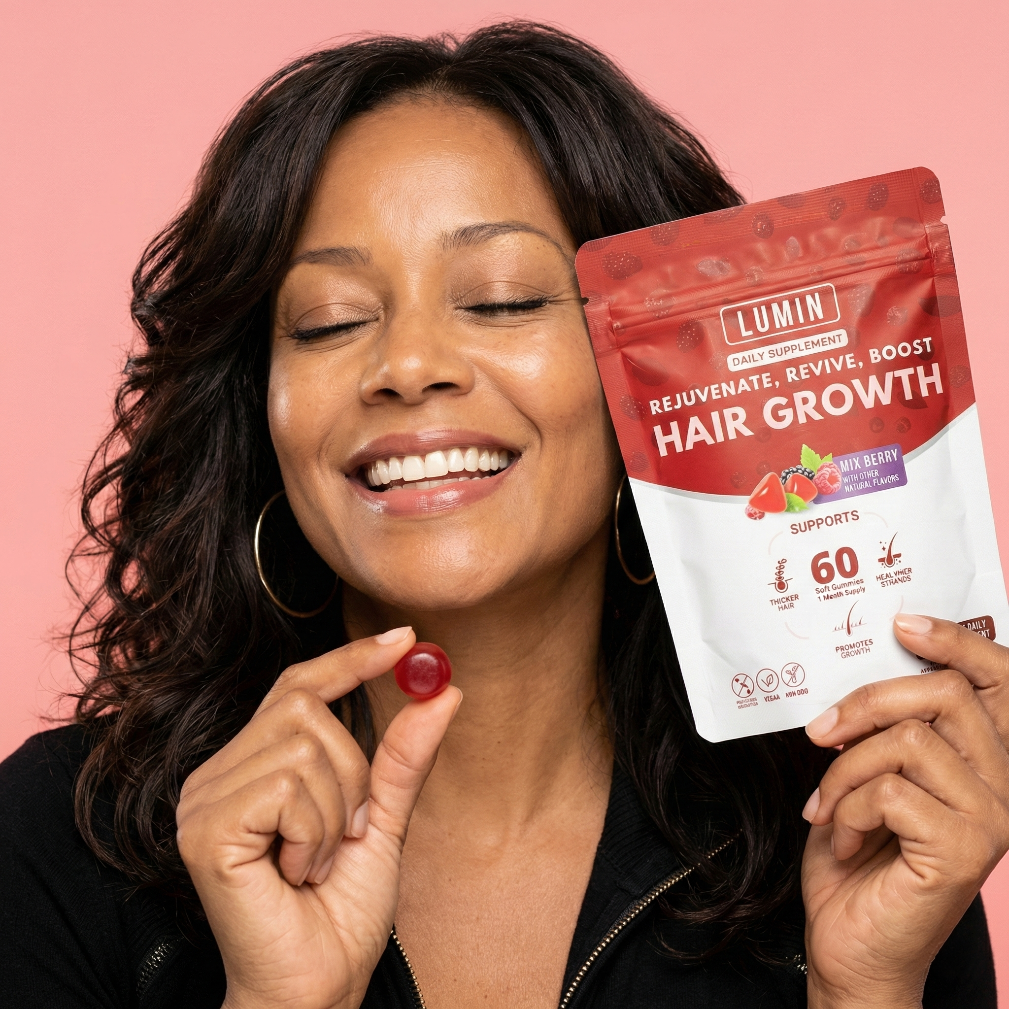 A woman with eyes closed smiles, holding a red gummy and a pouch of hair growth supplements.