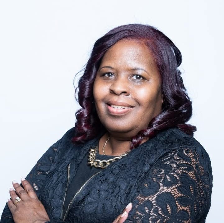 A person smiling with arms crossed, wearing a black lace outfit and necklace.