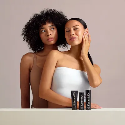 Two women standing with skincare tubes on a table.