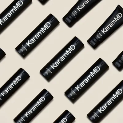 Black KaramMD bottles and tubes arranged on a beige background.