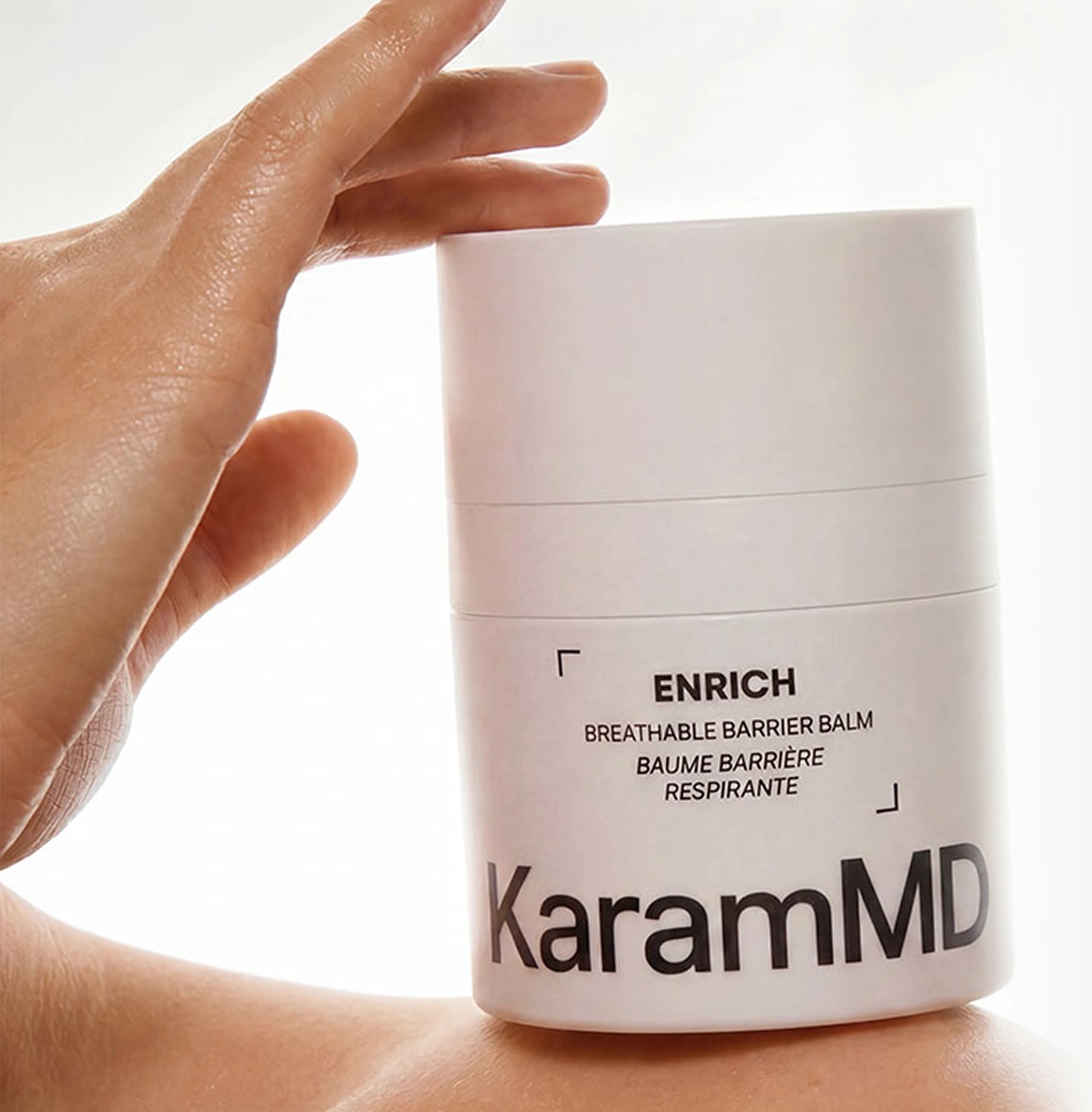 A hand holds a white jar of KaramMD Enrich Breathable Barrier Balm against a person's shoulder.