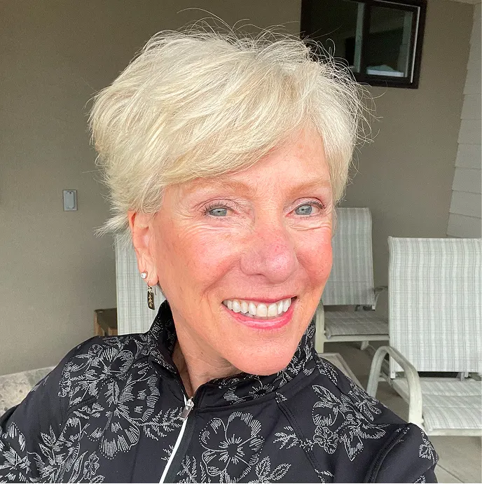 A smiling woman with short blonde hair wearing a black and white floral patterned jacket.