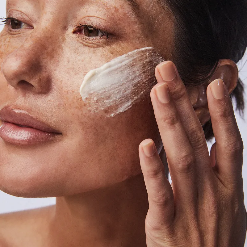Person applying cream to their cheek with fingers.