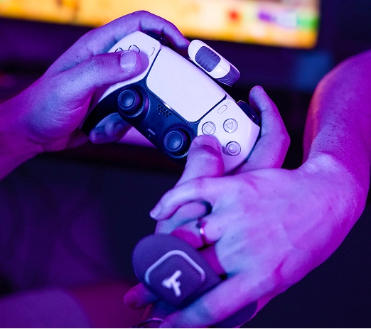 Two hands holding a gaming controller under purple lighting.