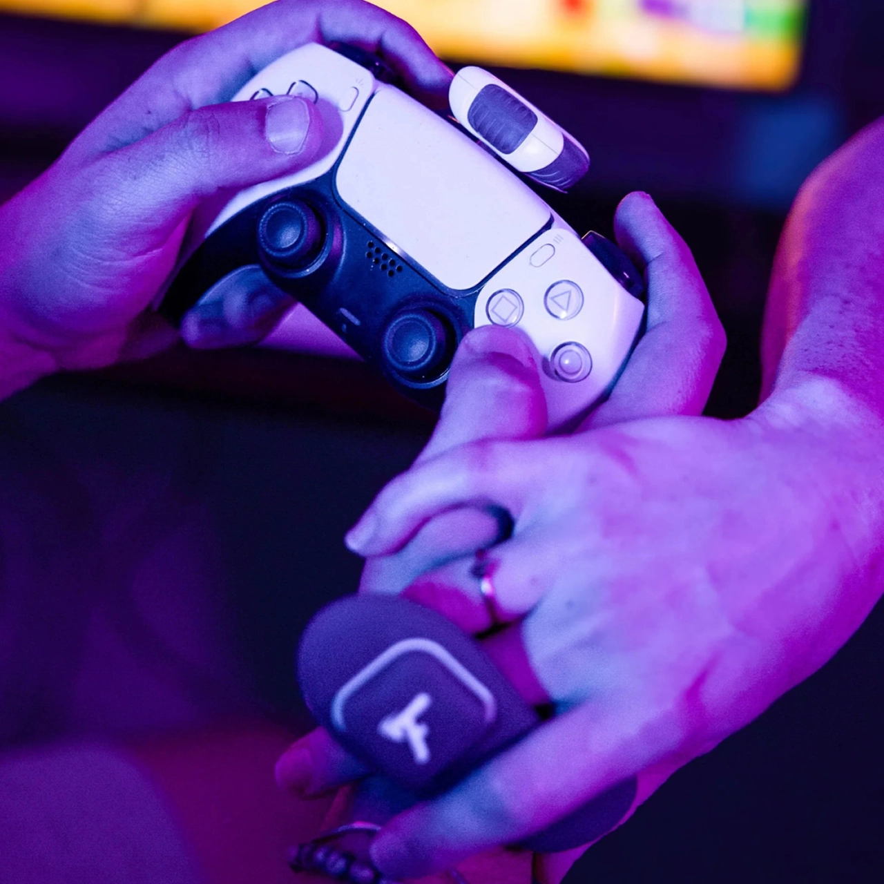 A close-up of a man's hands holding an Xbox controller with a Playmate plugged in and a woman's hand draped over holding a Fluffer panty vibrator