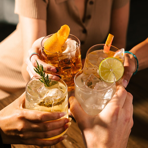 Four hands holding cocktails with garnishes, toasting together.