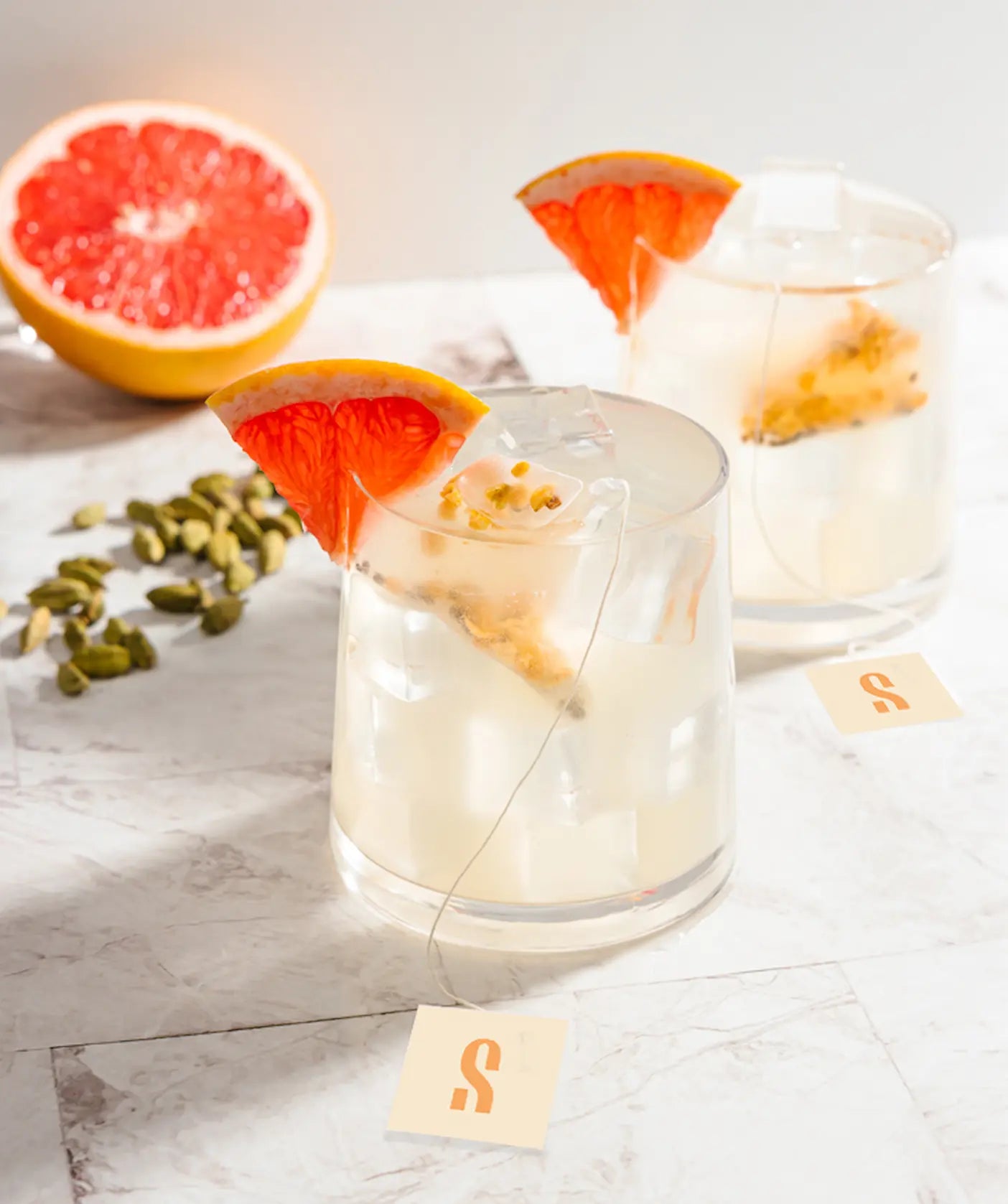 Two glasses of iced tea with grapefruit slices and cardamom pods.
