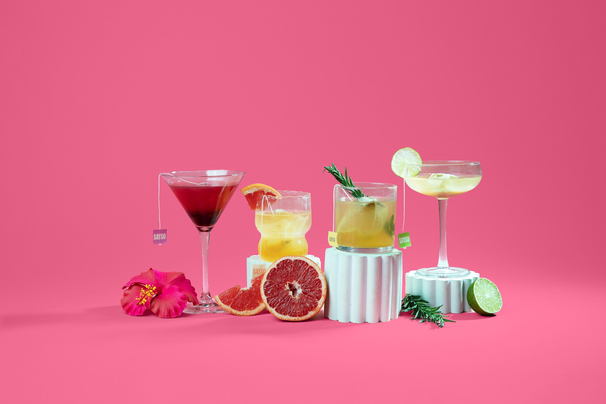 Four cocktails with garnishes on a pink background.