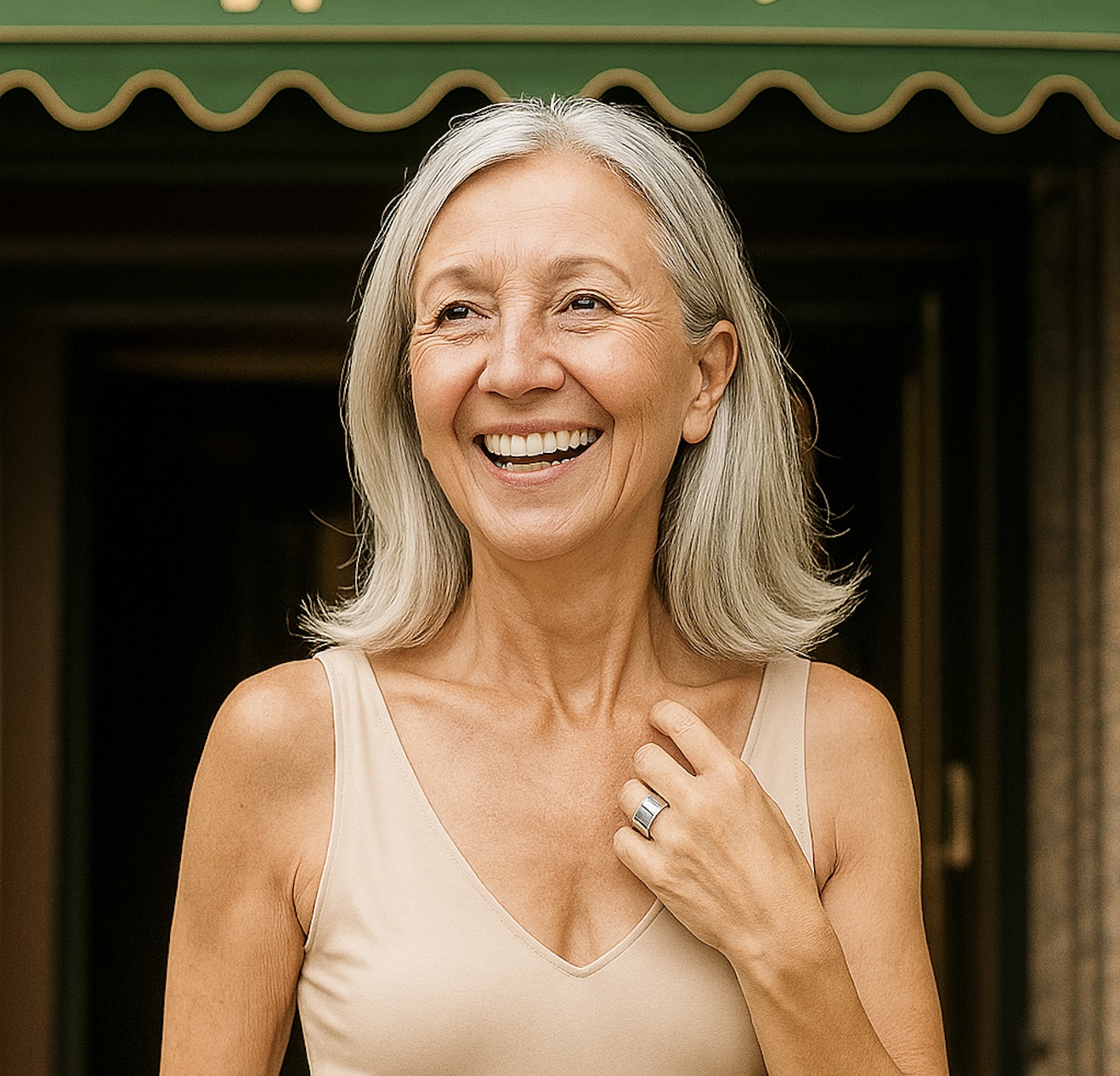 Smiling woman with gray hair wearing a beige top, standing outdoors.