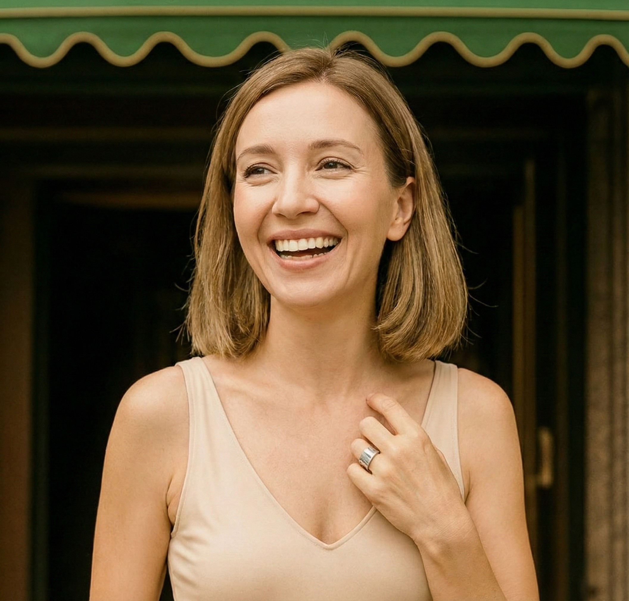 Smiling woman with gray hair wearing a beige top, standing outdoors.