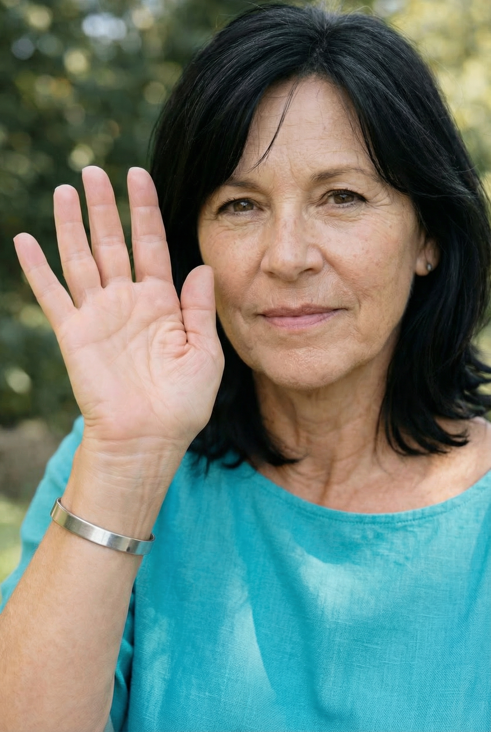 Woman in turquoise shirt raising her hand, outdoors.