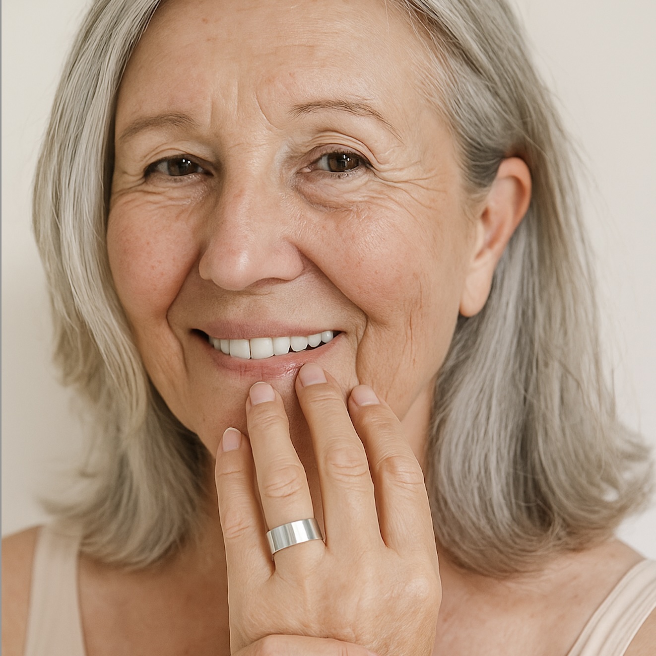 Smiling woman with gray hair touching her face, wearing a silver ring.