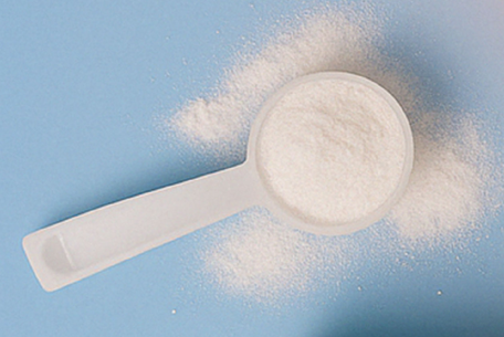 A white scoop filled with white powder, resting on a light blue surface with powder spilled around it.
