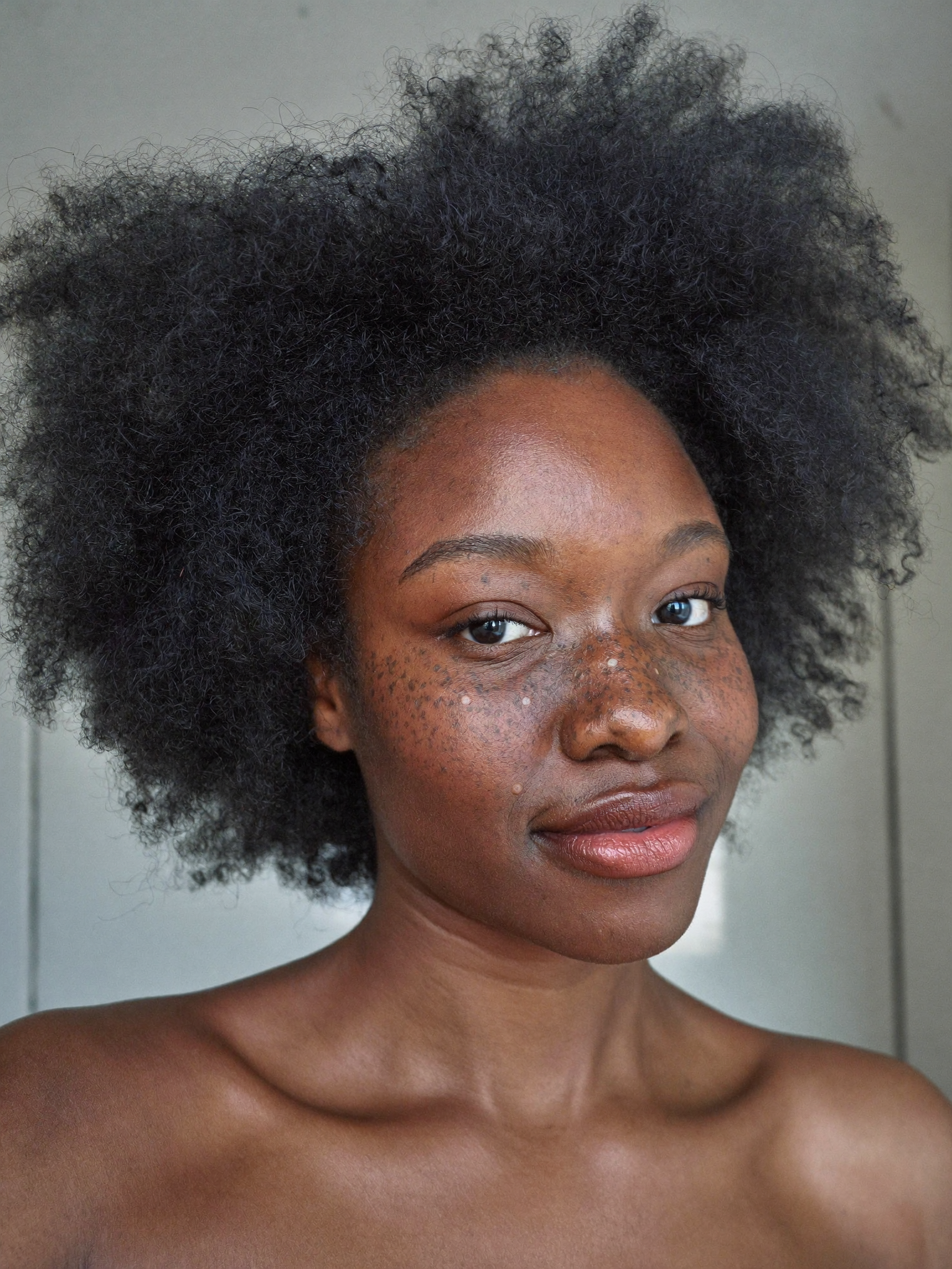 A close-up portrait of a Black woman with natural hair and freckles, looking at the camera.