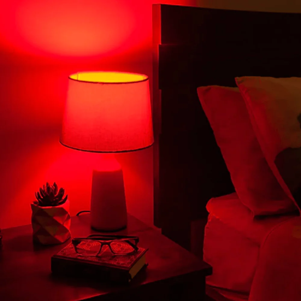 Red-lit bedside table with lamp, book, glasses, and plant.