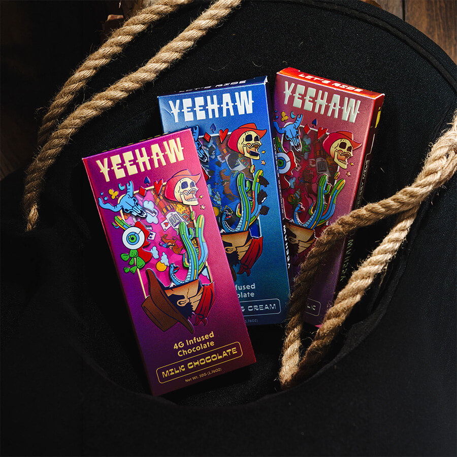 Three Yeehaw-branded packages with psychedelic western art floating over a desert highway under a pastel sky.