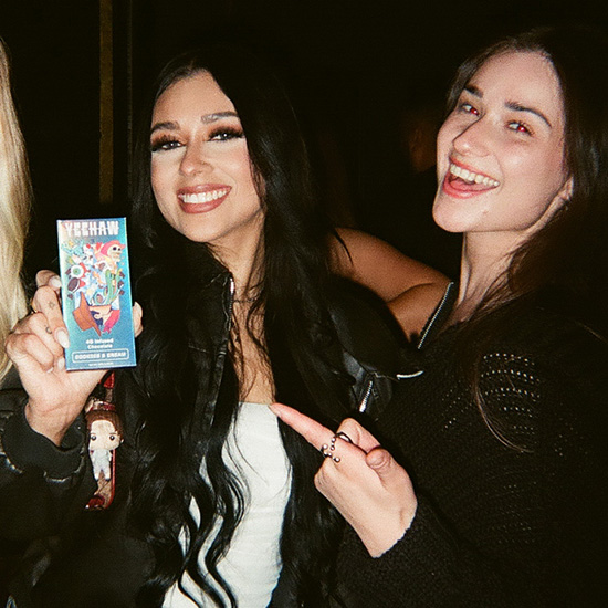 Two women smiling, one holding a Yeehaw chocolate bar while the other points at it.