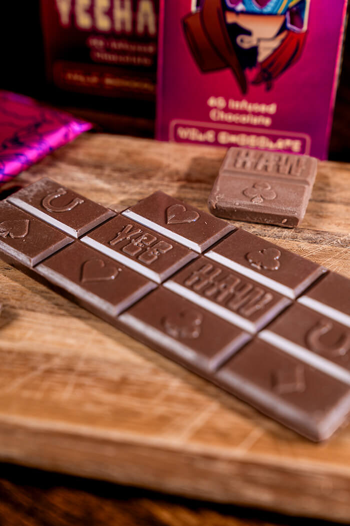 Three illustrated Yeehaw chocolate bars floating over a desert road leading to a celestial rock archway.