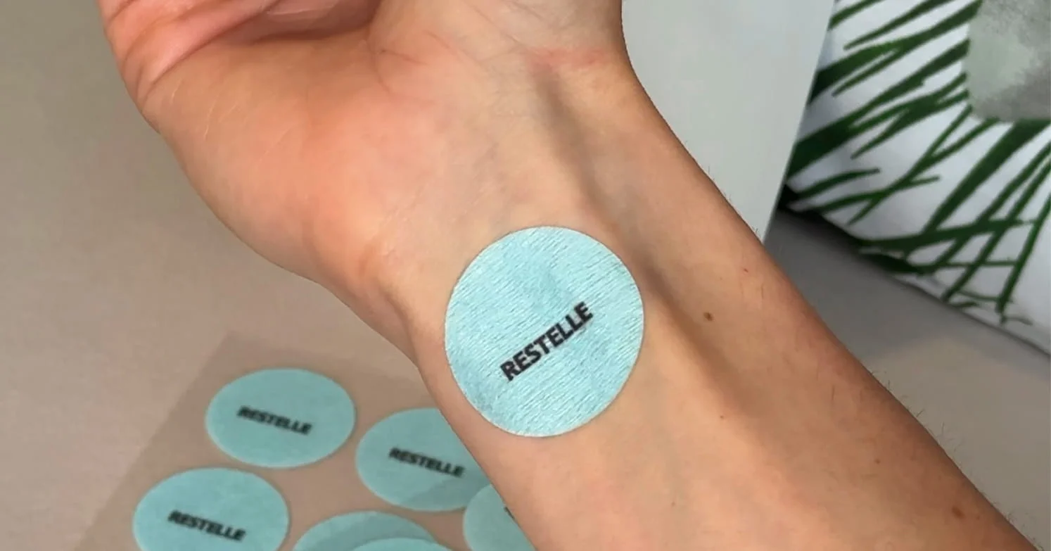 A close-up of a person's wrist with a light blue, circular patch that says 'RESTELLE' on it.